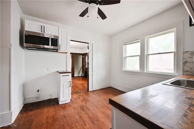 kitchen featuring stainless steel microwave, white cabinetry, a ceiling fan, wood finished floors, and baseboards