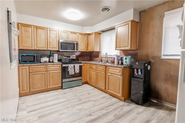 kitchen with stainless steel appliances, light wood-type flooring, decorative backsplash, and a sink