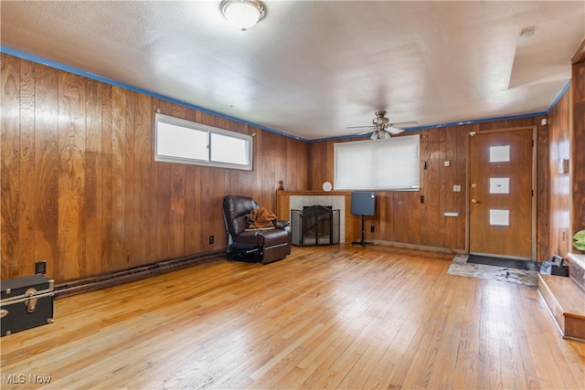unfurnished room with a tiled fireplace, wood-type flooring, ceiling fan, and wood walls