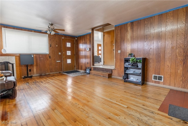 living area featuring wood finished floors, ceiling fan, wooden walls, and baseboards
