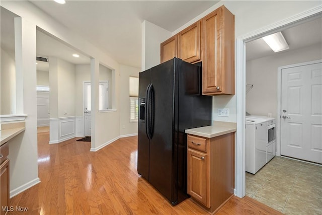 kitchen with black refrigerator with ice dispenser, washing machine and clothes dryer, light countertops, light wood finished floors, and brown cabinetry