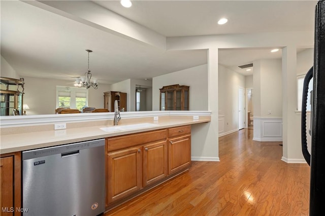 kitchen with stainless steel dishwasher, a sink, brown cabinets, a chandelier, and light countertops