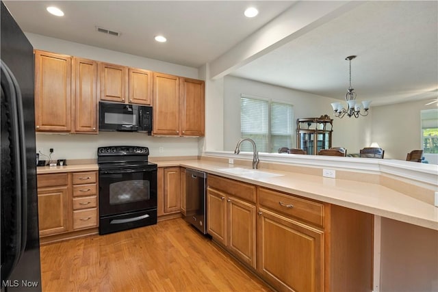 kitchen featuring black appliances, a sink, light wood-style flooring, a peninsula, and light countertops