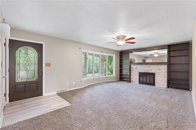 unfurnished living room with carpet floors, ceiling fan, a textured ceiling, baseboards, and a fireplace