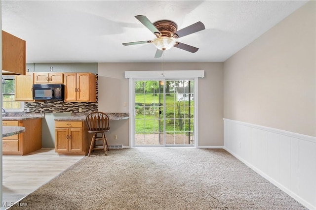 kitchen featuring black microwave, decorative backsplash, a ceiling fan, light carpet, and wainscoting