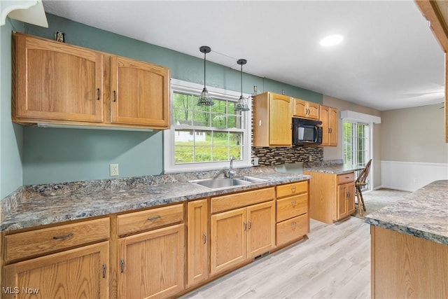 kitchen with black microwave, a sink, light wood-style floors, pendant lighting, and decorative backsplash