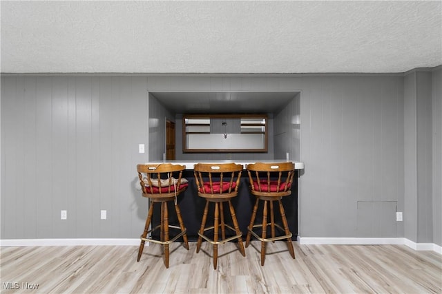 indoor dry bar featuring wood finished floors, baseboards, and a textured ceiling