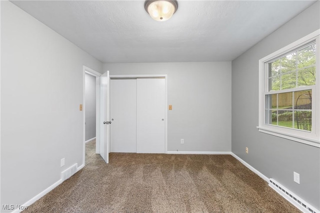 unfurnished bedroom with baseboard heating, carpet floors, a closet, and baseboards