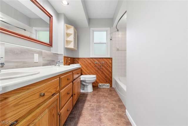 bathroom with wainscoting, toilet, double vanity, wood walls, and shower / bath combination