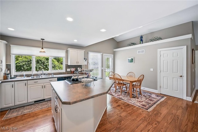 kitchen with a sink, white cabinets, wood finished floors, a kitchen island, and recessed lighting