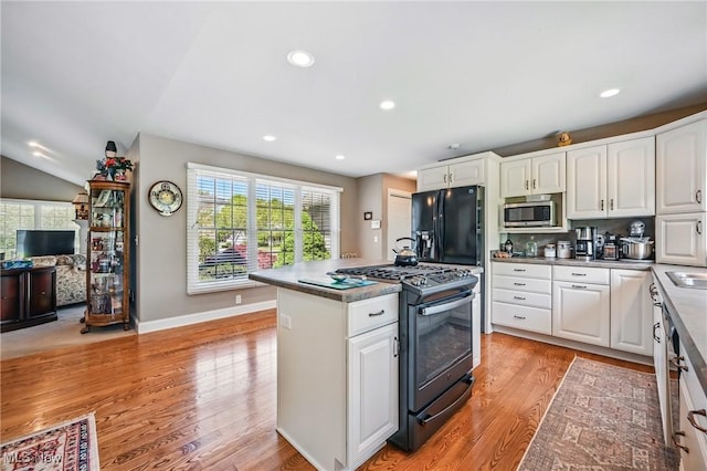 kitchen with black range with gas stovetop, stainless steel microwave, white cabinets, light wood-type flooring, and recessed lighting