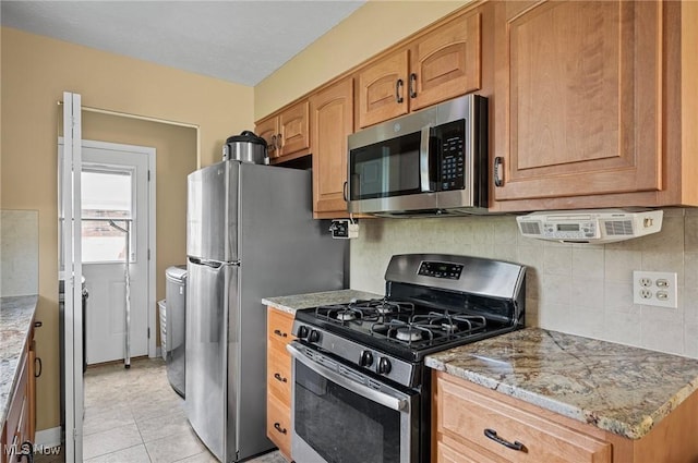 kitchen with appliances with stainless steel finishes, tasteful backsplash, light tile patterned floors, and light stone countertops