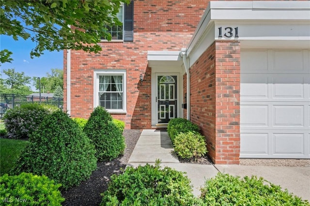 property entrance with a garage, fence, and brick siding