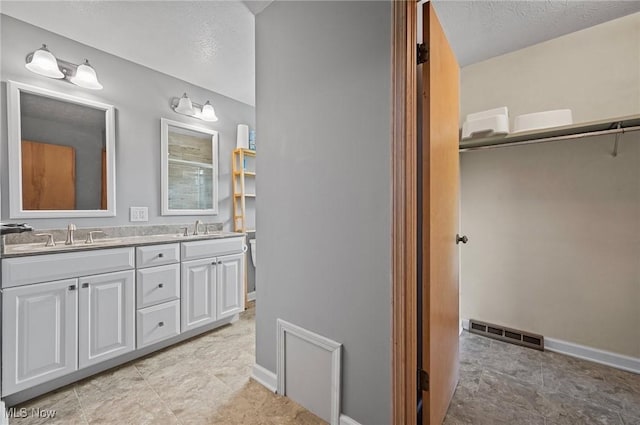 full bathroom featuring double vanity, a textured ceiling, baseboards, and a shower