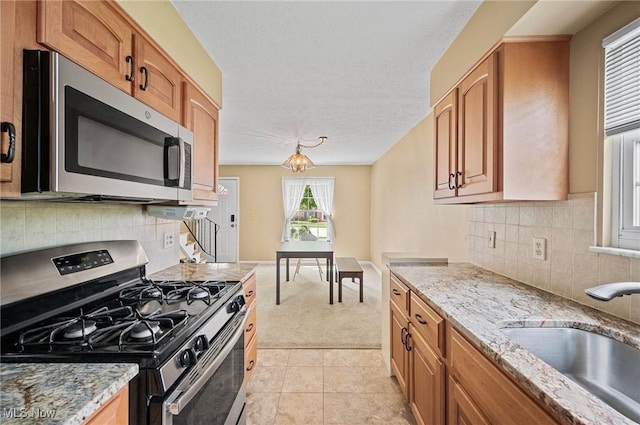 kitchen with appliances with stainless steel finishes, a sink, light colored carpet, light stone counters, and a textured ceiling