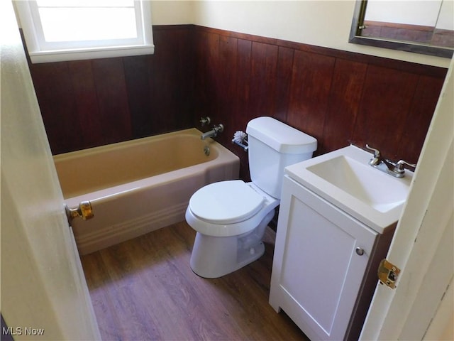 full bathroom with wood finished floors, a tub to relax in, toilet, vanity, and wooden walls