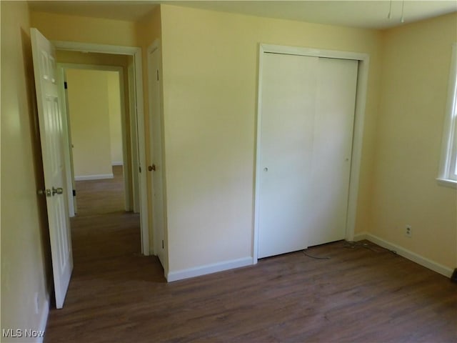 unfurnished bedroom featuring dark wood-style flooring, a closet, and baseboards