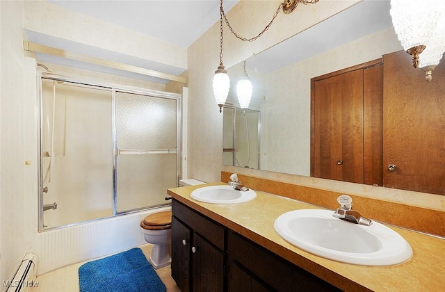 bathroom with a baseboard heating unit, toilet, combined bath / shower with glass door, and double vanity