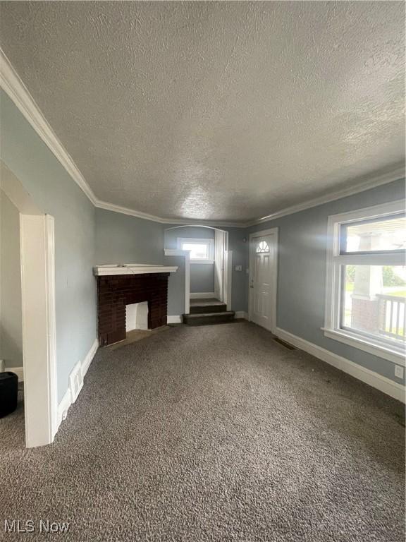 unfurnished living room with a textured ceiling, crown molding, carpet, stairway, and baseboards