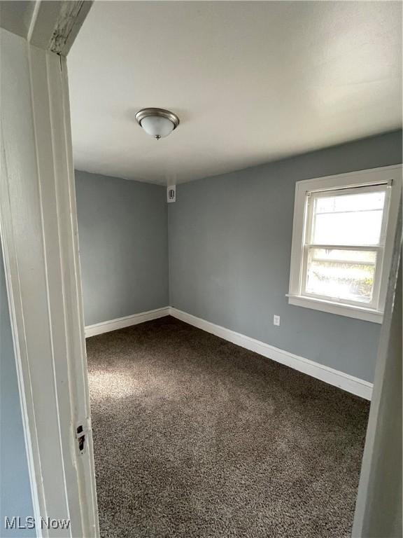 empty room with baseboards and dark colored carpet
