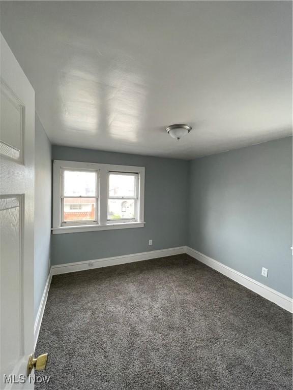 unfurnished room with dark carpet and baseboards
