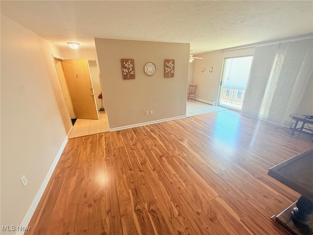 spare room featuring light wood finished floors, a baseboard heating unit, baseboards, and a textured ceiling