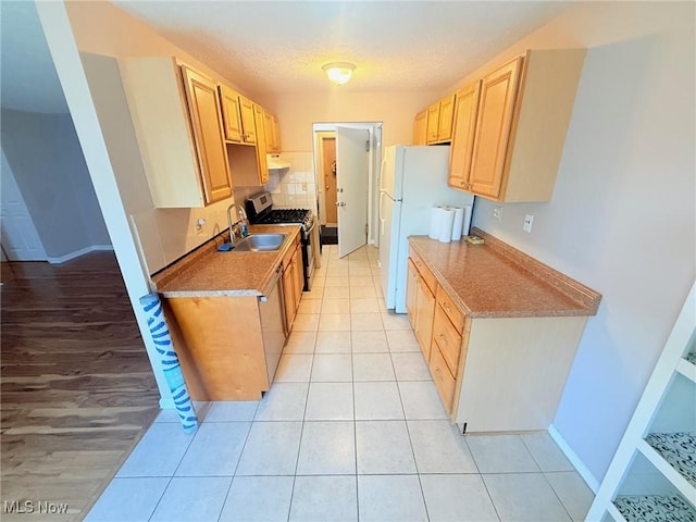 kitchen featuring gas stove, light brown cabinetry, a sink, freestanding refrigerator, and light tile patterned flooring
