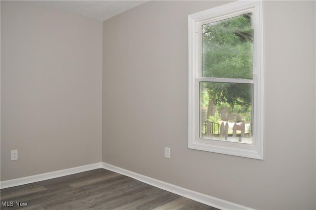empty room featuring plenty of natural light, baseboards, and dark wood-type flooring