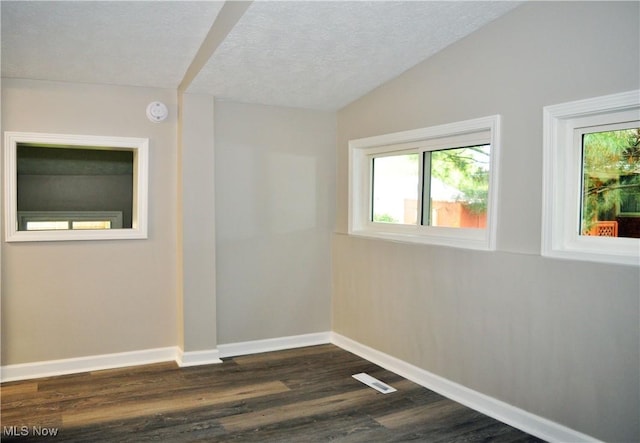 empty room featuring dark wood finished floors, baseboards, a textured ceiling, lofted ceiling, and a smoke detector