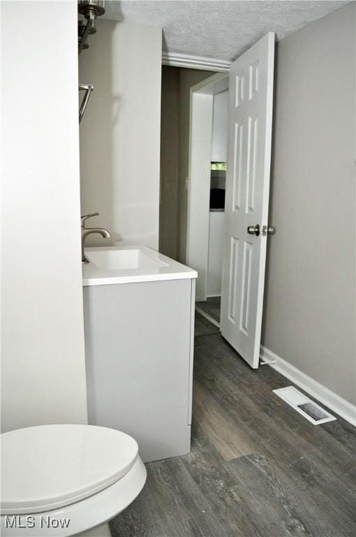 bathroom with wood finished floors, toilet, vanity, a textured ceiling, and baseboards