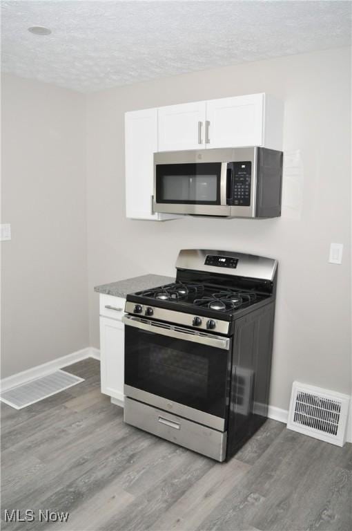 kitchen with appliances with stainless steel finishes, light wood-type flooring, baseboards, white cabinetry, and a textured ceiling