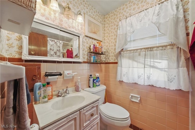 bathroom with wallpapered walls, toilet, wainscoting, a shower with shower curtain, and tile walls