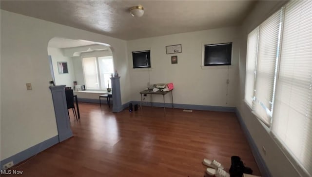 empty room with arched walkways, wood finished floors, and baseboards