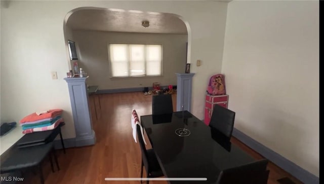 dining space with arched walkways, wood finished floors, and baseboards