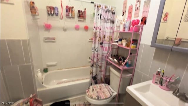 full bath featuring tile walls, shower / tub combo with curtain, toilet, a sink, and wainscoting