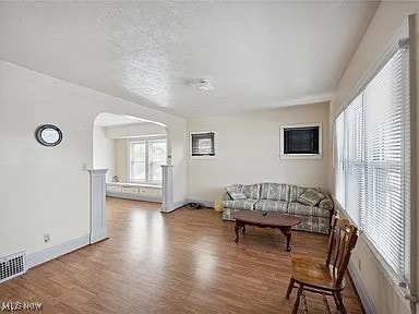 living area with arched walkways, wood finished floors, baseboards, and a textured ceiling