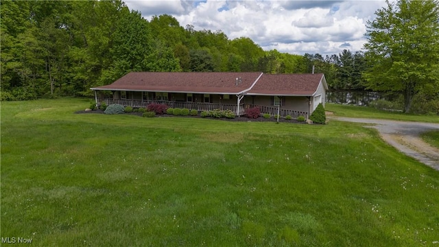 view of front of property with covered porch, a wooded view, a front yard, and dirt driveway