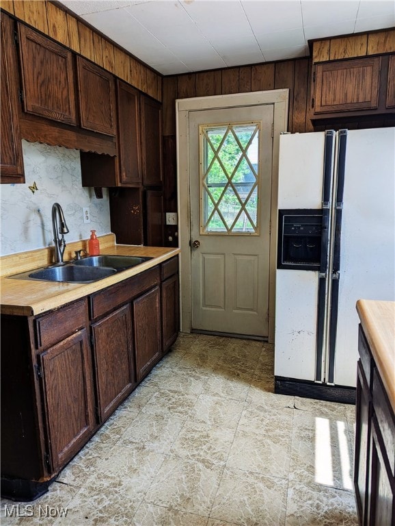 kitchen featuring white refrigerator with ice dispenser, a sink, light countertops, and dark brown cabinetry