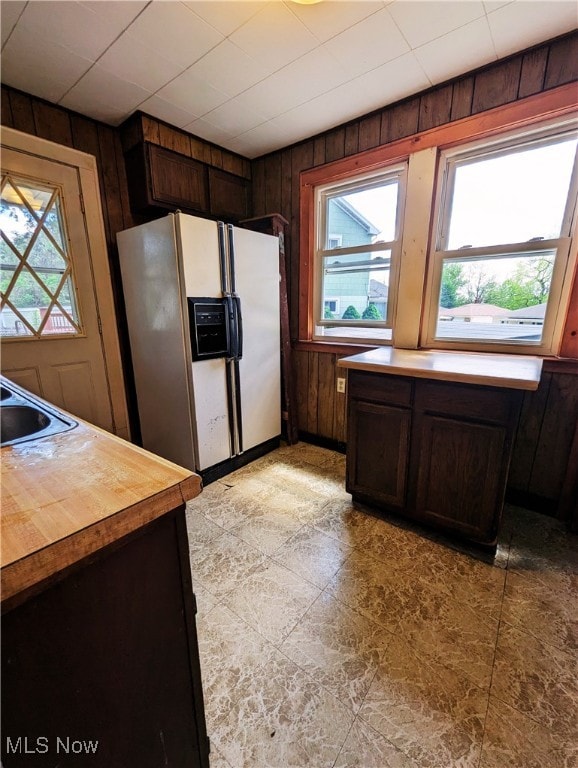 kitchen with white refrigerator with ice dispenser, wood walls, a sink, dark brown cabinets, and butcher block countertops