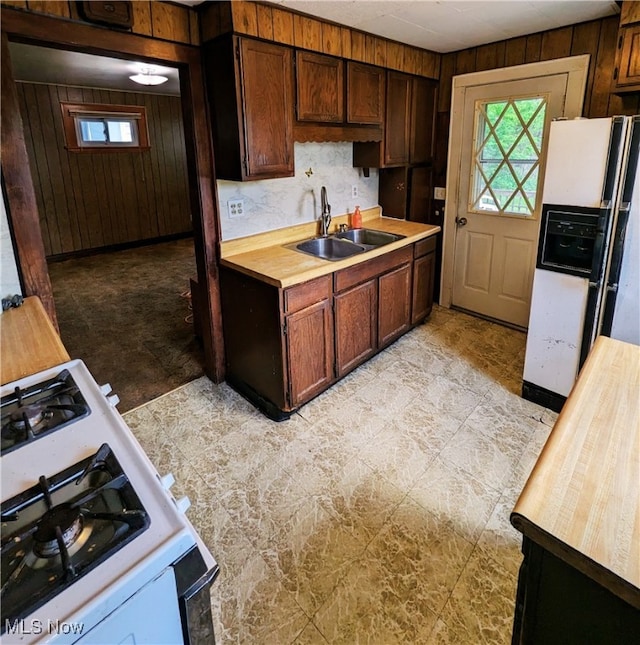 kitchen featuring a sink, white appliances, butcher block counters, wooden walls, and healthy amount of natural light