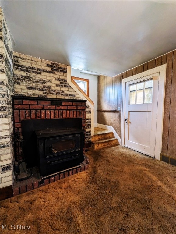 living area with carpet, wooden walls, a wood stove, stairs, and baseboards