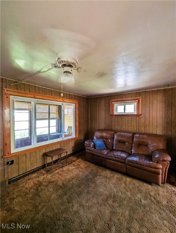 carpeted living room with wood walls and ceiling fan