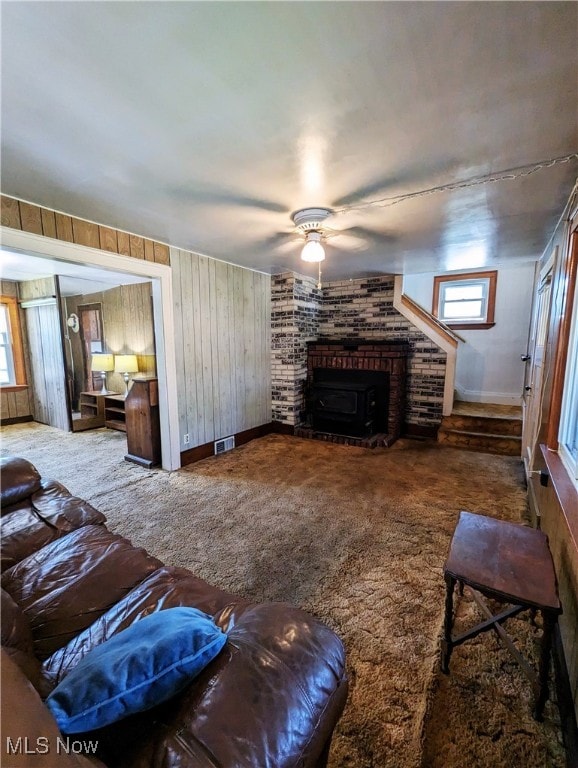 carpeted living room featuring a ceiling fan, wooden walls, and a brick fireplace