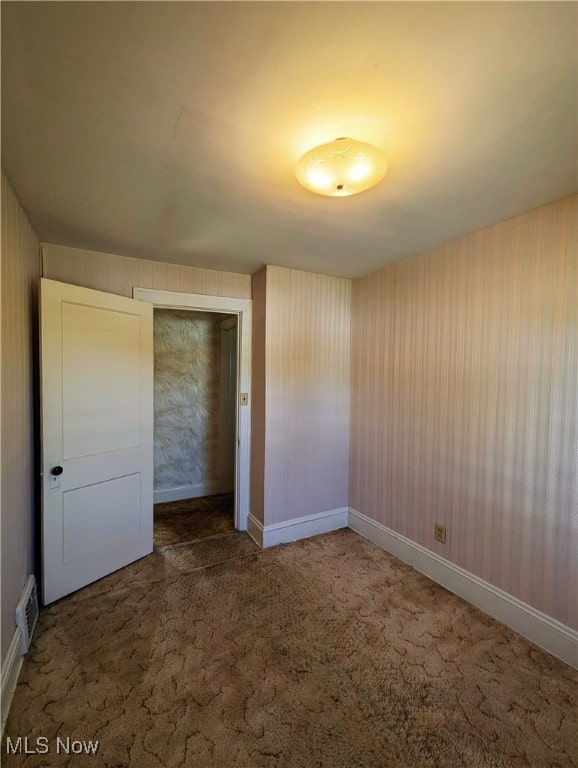 unfurnished bedroom with wallpapered walls, carpet flooring, baseboards, and a closet