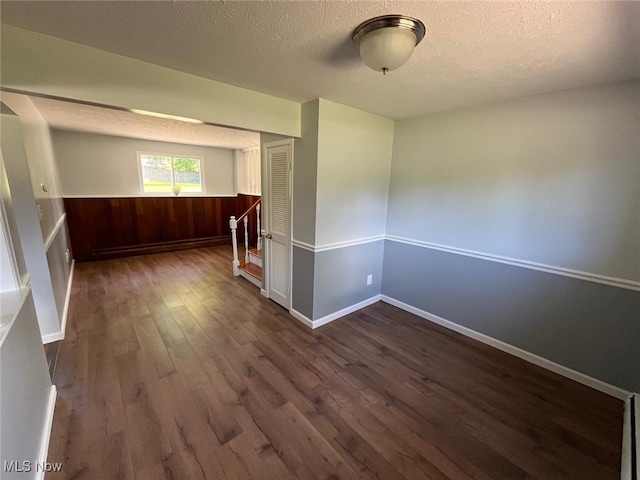 5135 Berkshire Dr, North Olmsted, OH 44070 - empty room featuring dark wood finished floors, a textured ceiling, wainscoting, wood walls, and baseboards