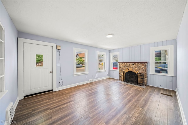 579 Main St, Conneaut, OH 44030 - unfurnished living room featuring a textured ceiling, wood finished floors, a stone fireplace, and baseboards