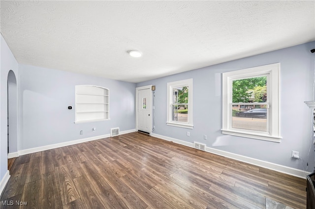 579 Main St, Conneaut, OH 44030 - unfurnished living room featuring arched walkways, a textured ceiling, wood finished floors, baseboards, and built in features