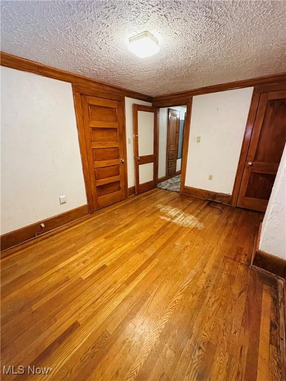 unfurnished room featuring light wood-type flooring, a textured ceiling, baseboards, and crown molding