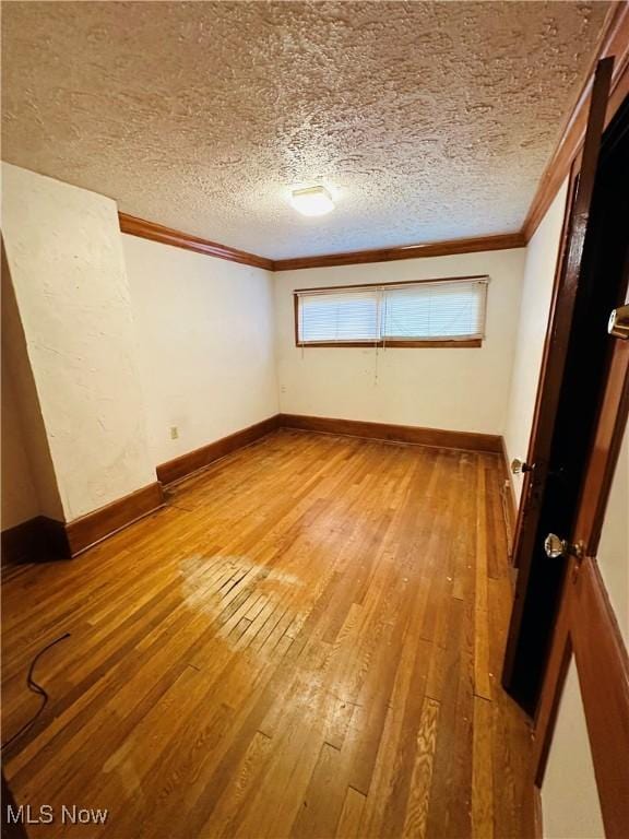 unfurnished bedroom with crown molding, light wood finished floors, a textured ceiling, and baseboards