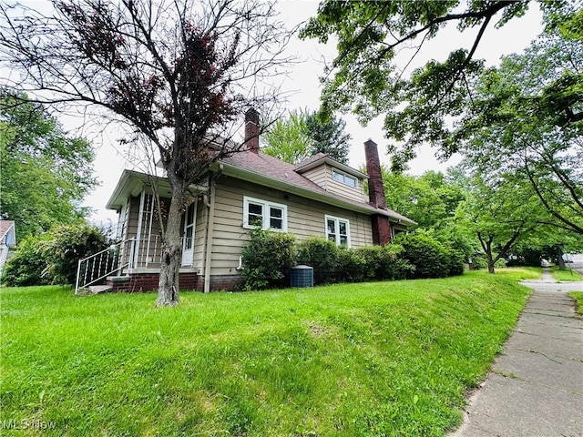 view of side of property with a chimney, a lawn, and central AC